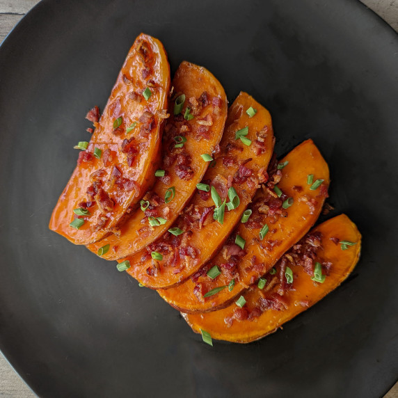 A plate of maple bourbon glazed sweet potato wedges topped with crumbled bacon and chives