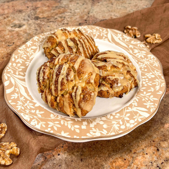 Maple walnut scones stacked on a white plate with a brown flowered edging with one cut in half.