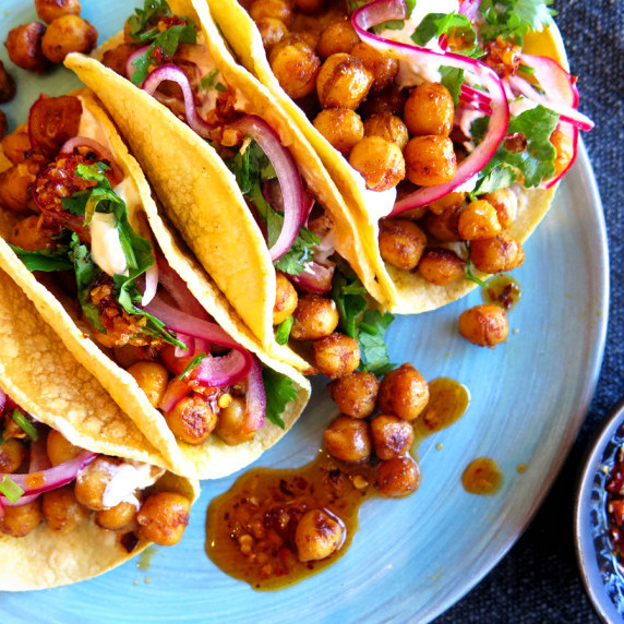 Masala chickpea tacos, topped with pickled red onion, cilantro, and spice arranged on a blue plate.