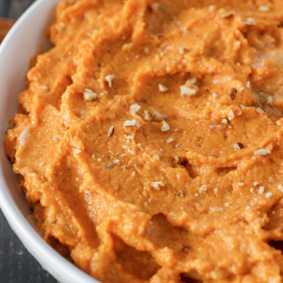Mashed Sweet Potatoes in a white bowl with pecans sprinkled on top