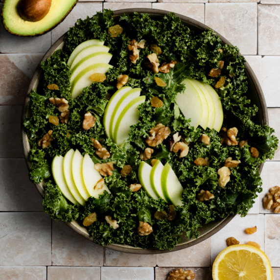 massaged kale avocado salad arranged in an aesthetic plate with avocado and orange on the side