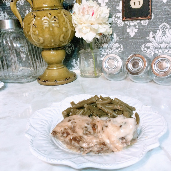 Meatloaf with gravy plated with green beans on a white scalloped plate on top of marble countertop