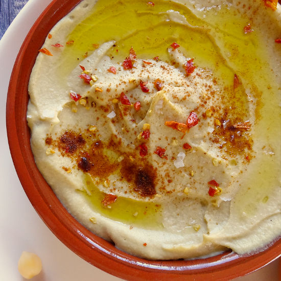 An earthenware dish sits filled with Mediterranean hummus topped with olive oil and paprika
