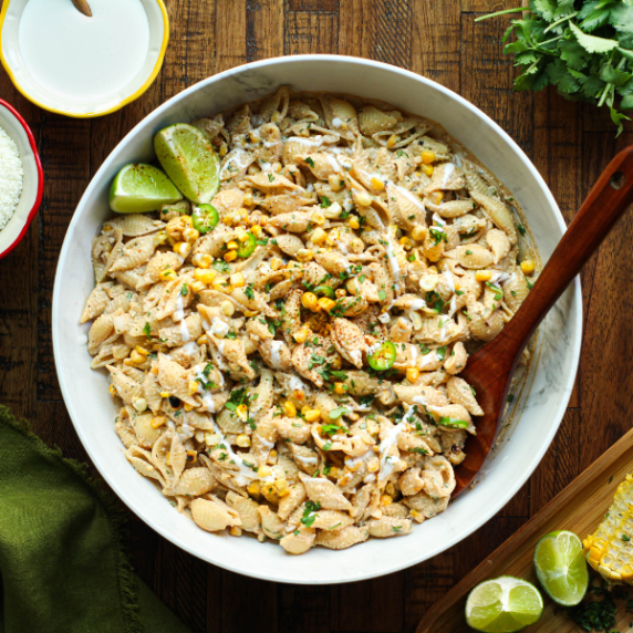 Mexican street corn pasta salad in a white bowl with a wooden spoon.