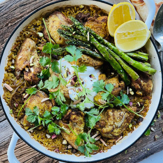 white baking dish filled with Middle Eastern chicken and rice topped with herbs, lemon and asparagus