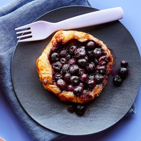 A blueberry galette on it's own plate with a fork and napkin.