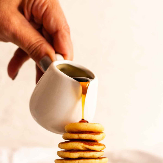 Pouring maple syrup over a  stack of mini pancakes.