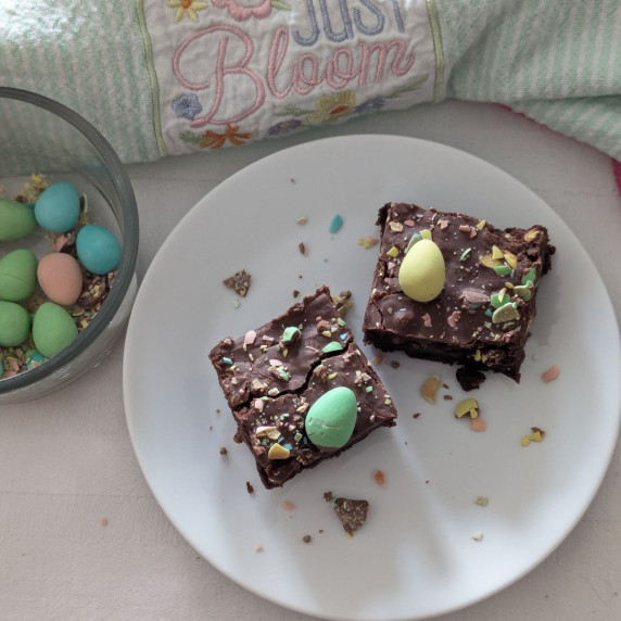 Two frosted mini egg brownies on a plate with a bowl of mini eggs off to the left side.