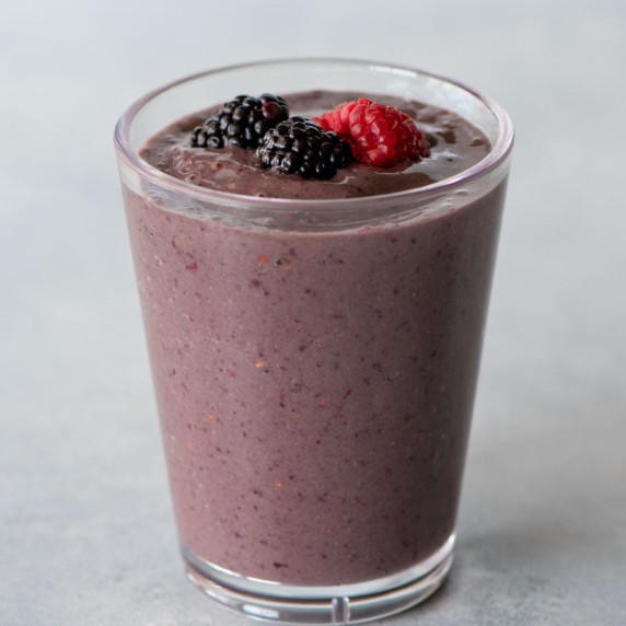 A mixed berry smoothie topped with fresh berries in a tall glass on a light background.