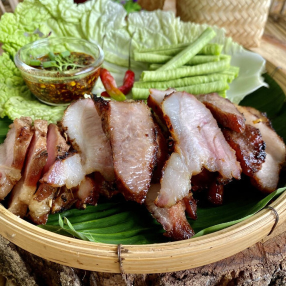 Thai grilled pork slices with a chili dipping sauce and fresh vegetables.