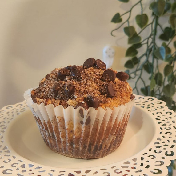  A hand presents a muffin with streusel and chocolate chips on a patterned plate, against a floral b
