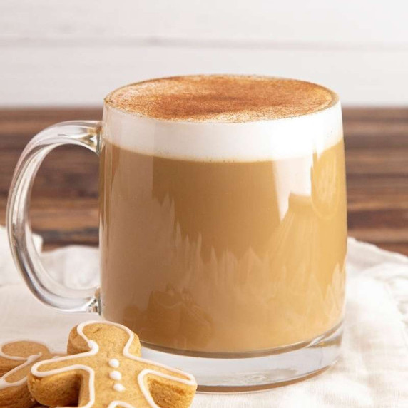 Homemade gingerbread latte in a glass mug with two gingerbread cookies beside it.