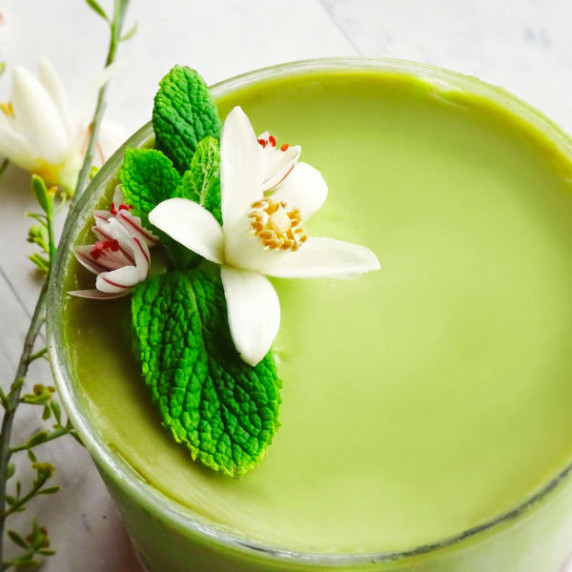 A small glass is filled with bright green avocado and mint cheesecake and is garnished with mint