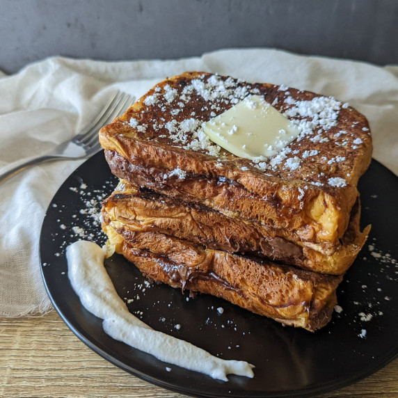 A stack of Nutella stuffed brioche french toast topped with butter and powdered sugar