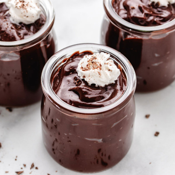 Oat milk chocolate pudding in glass jars with whip topping on top.