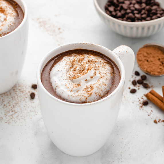 Oat milk hot chocolate in a white mug with coconut whip and cinnamon on top.