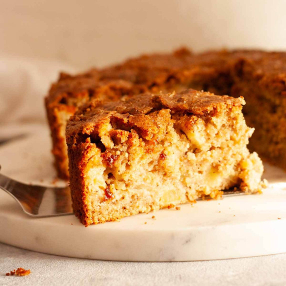 A slice of oatmeal apple cake on a white marble platter.