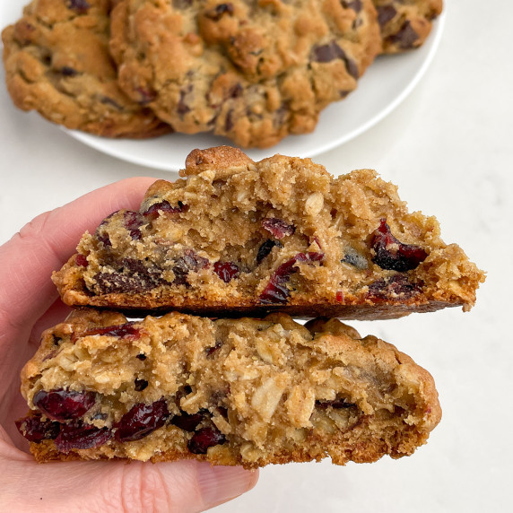 An oatmeal craisin cookie broken in half and a plate of oatmeal craisin cookies. 