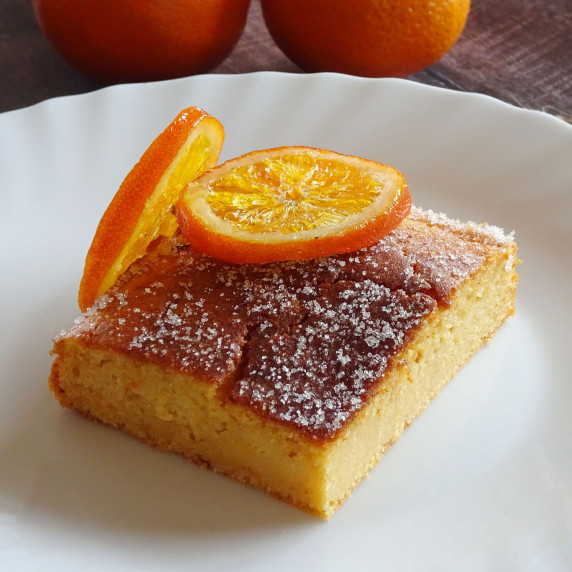 A slice of orange and pink grapefruit cake sits on a white plate with a sprinkling of sugar