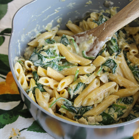 A pot of creamy spinach and artichoke pasta with a wooden spoon