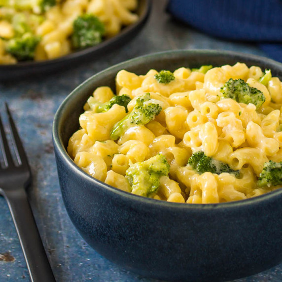 Side close up shot of Mac and cheese with broccoli in a black bowl on a blue speckled surface.
