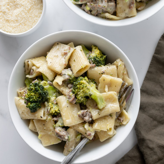 rigatoni pasta with broccoli and sausage in a white bowl with a green napkin.