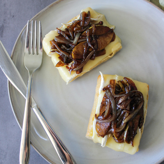 An open faced sandwich with baked brie and caramelized apples and onions served on a plate