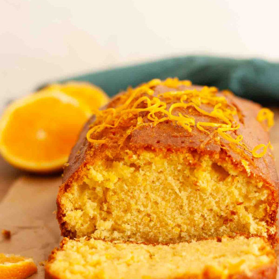 A close up of an orange loaf cake sliced next to sliced oranges.