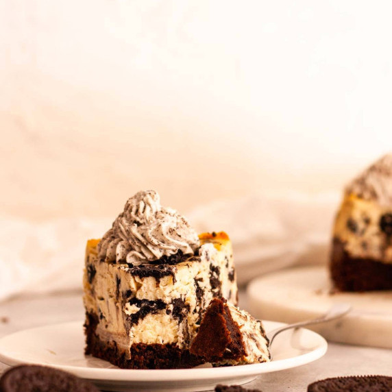 A slice of Oreo Brownie Cheesecake on a white plate with a fork.
