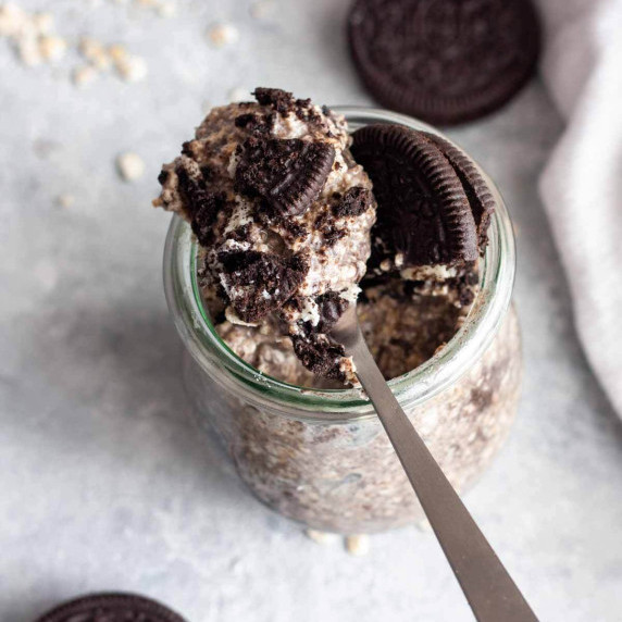 Oreo overnight oats on a spoon over a jar next to oats and oreo cookies.