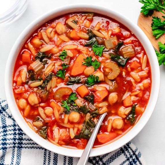 Vegetable orzo soup with chickpeas in a white bowl with a spoon.