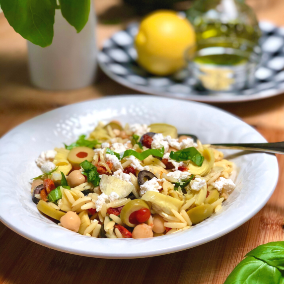 A white bowl filled with vegan lemon artichoke orzo salad with olives & chickpeas. 