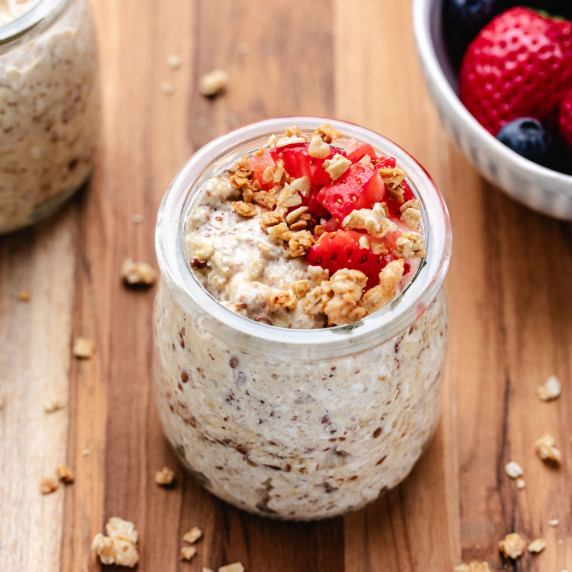 Overnight oats with water in a glass jar with diced strawberries and granola on top.