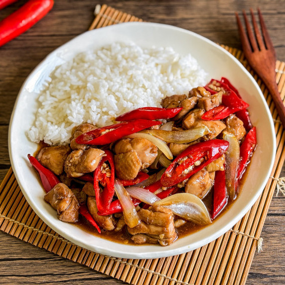 Top-view of Thai chili chicken stir-fry with onion and a side of jasmine rice.