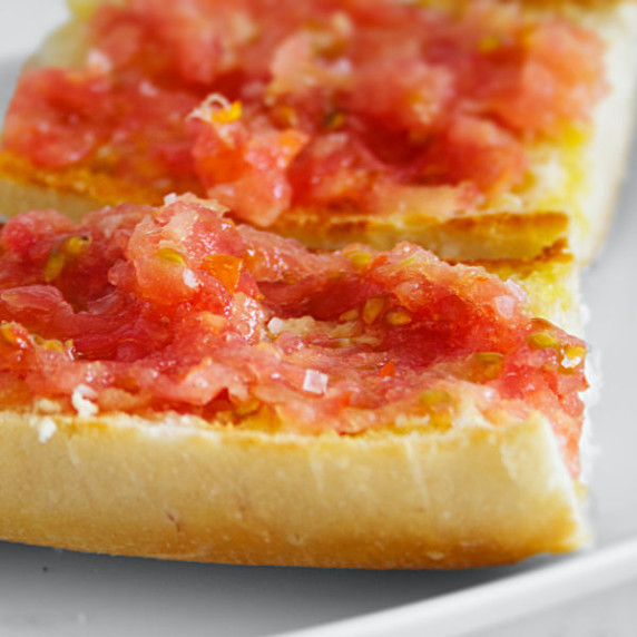 two slices of pan con tomate sit on a white plate with some olive oil and salt 