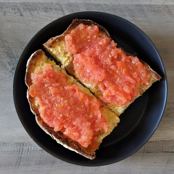 Two pieces of toasted bread topped with grated tomato and olive oil