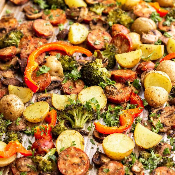 Roasted vegetables and sausage coins on a baking sheet garnished with chopped fresh parsley.