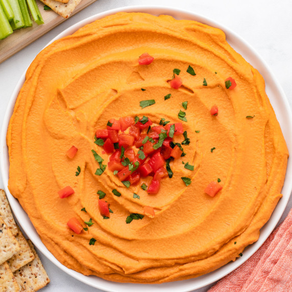 Smoked paprika hummus spread on a plate with diced roasted red peppers on top.