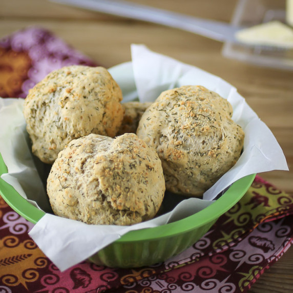 Side shot of multiple biscuits in a green bowl lined with parchment paper on a colorful cloth.