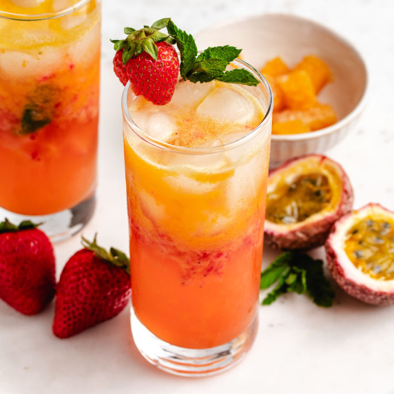 A passion fruit mocktail in a glass with a strawberry and mint.