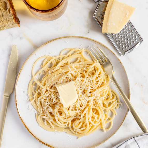 A bowl of Butter Parmesan Pasta topped with melted butter and grated Parmesan, served in a deep whit