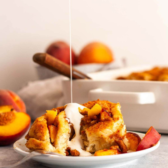 Cream poured over a peach cinnamon roll on a white plate.