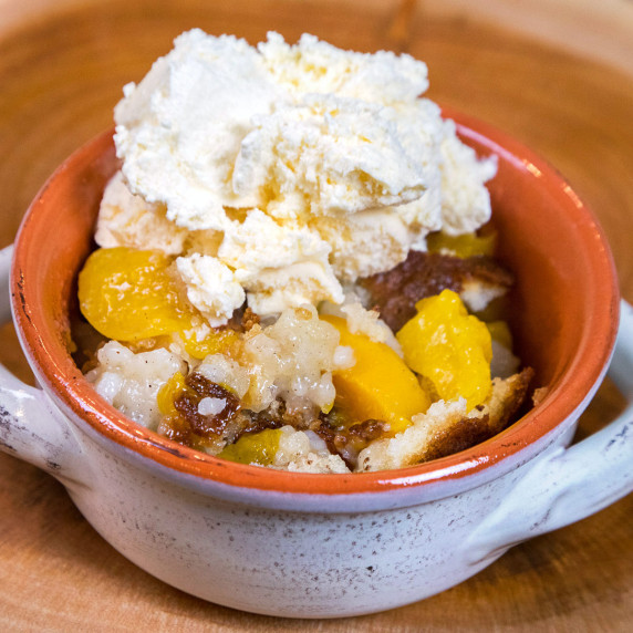 Peach cobbler in a bowl topped with vanilla ice cream.