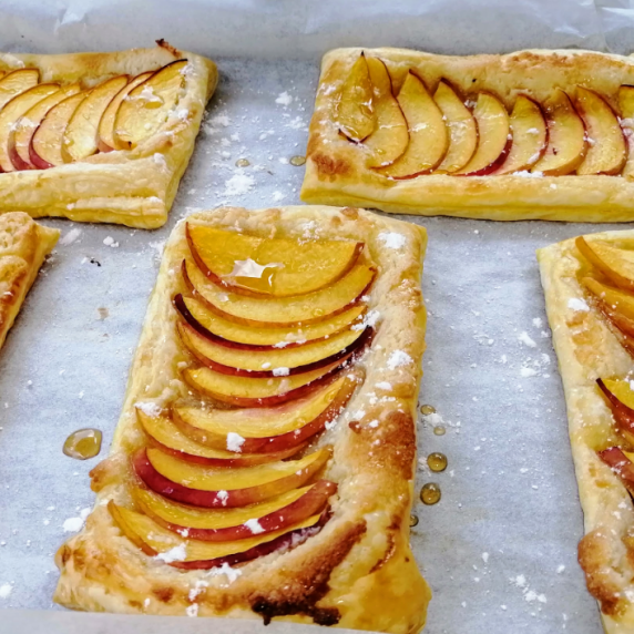 Peach tarts on a parchment paper lined baking sheet.