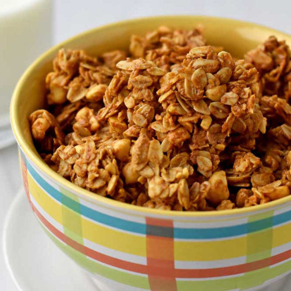A multi-colored bowl filled with peanut butter granola with a glass of milk in the background.