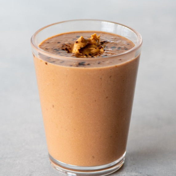 A chocolate peanut butter smoothie in a tall glass garnished with a dollop of peanut butter.