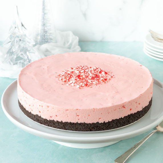 Frozen Chocolate Peppermint Cheesecake on a white cake stand, with glass trees in the background
