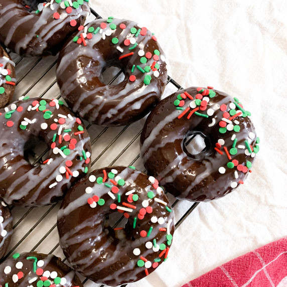 Peppermint Mocha Donuts with white chocolate drizzle and sprinkles on a cooling rack