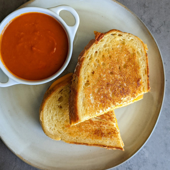 A perfectly golden brown grilled cheese sandwich served with tomato soup