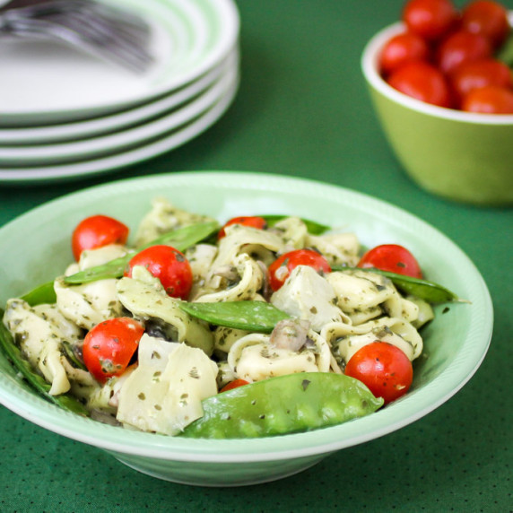 Side view of pesto tortellini in a green bowl with plates and a green bowl in the background.